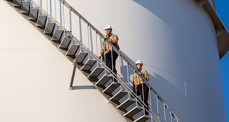 Zwei BASF-Mitarbeiter mit Helm gehen Stufen entlang eines riesigen Silos hinauf (Foto)